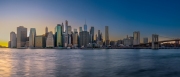 Panoramic cityscape about lower Manhattan's skyscrapers.  The photo taken from brooklyn bridge park. Amazing blue hour view and the sundown on the left side, 
Old pier's columns on the foreground.