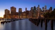 Panoramic cityscape about lower Manhattan's skyscrapers.  The photo taken from brooklyn bridge park. Amazing blue hour view and the sundown on the left side, 
Old pier's columns on the foreground.