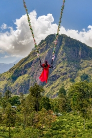A woman swings high above the lush hills of Ella, Sri Lanka, with Little Adam’s Peak in the background, enjoying a thrilling and scenic adventure in nature