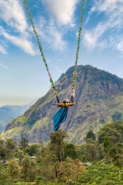 A woman swings high above the lush hills of Ella, Sri Lanka, with Little Adam’s Peak in the background, enjoying a thrilling and scenic adventure in nature