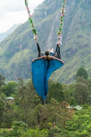 A woman swings high above the lush hills of Ella, Sri Lanka, with Little Adam’s Peak in the background, enjoying a thrilling and scenic adventure in nature