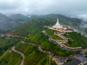 The image captures the Mahamevnawa Buddhist Monastery in Ella, Sri Lanka, perched atop a lush green hill surrounded by misty mountains. This sacred site is a serene place for meditation and prayer