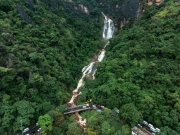The image captures the Secret Waterfall in Illukpelessa, Sri Lanka, surrounded by dense tropical greenery. Water cascades over rugged rocks into a tranquil pool, creating a hidden paradise