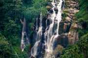 A stunning multi-tiered waterfall cascades down rocky cliffs in Ella, Sri Lanka, surrounded by lush greenery and terraced farmland, creating a serene natural escape.