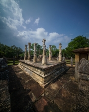 The image depicts the Vatadage, a circular relic house in Polonnaruwa’s Sacred Quadrangle, showcasing intricate stone carvings and ancient architecture under a clear sky