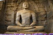 The image depicts the Vatadage, a circular relic house in Polonnaruwa’s Sacred Quadrangle, showcasing intricate stone carvings and ancient architecture under a clear sky