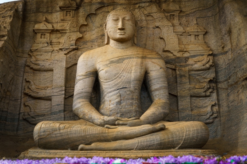 The image depicts the Vatadage, a circular relic house in Polonnaruwa’s Sacred Quadrangle, showcasing intricate stone carvings and ancient architecture under a clear sky