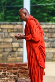 A Buddhist monk in a traditional red robe prays with devotion at an ancient site in Polonnaruwa, Sri Lanka, embodying spirituality and peaceful contemplation.