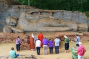 A group of devotees and monks pay respects at the ancient reclining Buddha statue in Polonnaruwa, Sri Lanka, a UNESCO heritage site carved from solid rock.