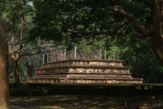 The image depicts the Vatadage, a circular relic house in Polonnaruwa’s Sacred Quadrangle, showcasing intricate stone carvings and ancient architecture under a clear sky