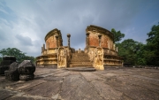 The image depicts the Vatadage, a circular relic house in Polonnaruwa’s Sacred Quadrangle, showcasing intricate stone carvings and ancient architecture under a clear sky