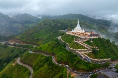 The image captures the Mahamevnawa Buddhist Monastery in Ella, Sri Lanka, perched atop a lush green hill surrounded by misty mountains. This sacred site is a serene place for meditation and prayer