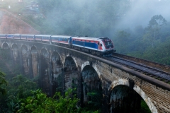 A scenic train crosses the iconic Nine Arch Bridge in Ella, Sri Lanka, surrounded by misty tropical forests, showcasing a blend of history, nature, and engineering marvel.