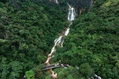The image captures the Secret Waterfall in Illukpelessa, Sri Lanka, surrounded by dense tropical greenery. Water cascades over rugged rocks into a tranquil pool, creating a hidden paradise