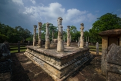 The image depicts the Vatadage, a circular relic house in Polonnaruwa’s Sacred Quadrangle, showcasing intricate stone carvings and ancient architecture under a clear sky