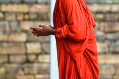A Buddhist monk in a traditional red robe prays with devotion at an ancient site in Polonnaruwa, Sri Lanka, embodying spirituality and peaceful contemplation.