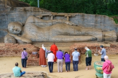A group of devotees and monks pay respects at the ancient reclining Buddha statue in Polonnaruwa, Sri Lanka, a UNESCO heritage site carved from solid rock.