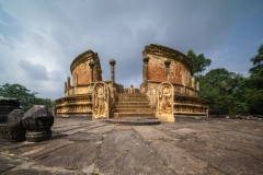 The image depicts the Vatadage, a circular relic house in Polonnaruwa’s Sacred Quadrangle, showcasing intricate stone carvings and ancient architecture under a clear sky