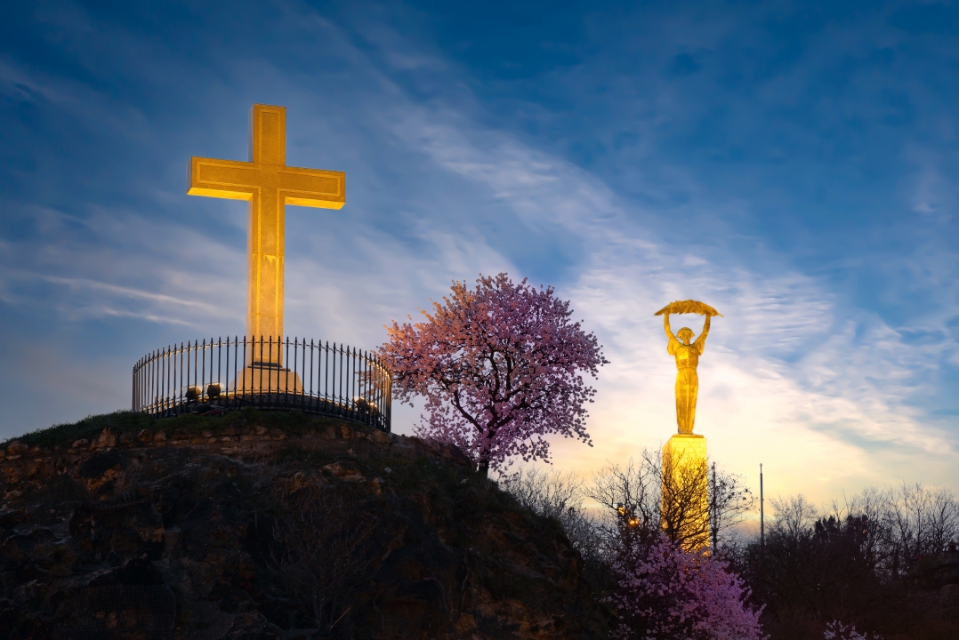 Christian cross with blooming tree and Liberty statue on the background in Gellert hill Budapest Hungary